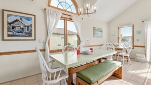 A dining area with a long table, white chairs, a bench, and a chandelier. - Terrapin Station: Private Pool | Oceanside (Corolla)