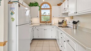 A kitchen with white cabinets, a stainless steel sink, and a window with a view of greenery. - Terrapin Station: Private Pool | Oceanside (Corolla)