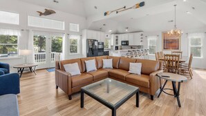 Un salon spacieux avec un canapé d’angle marron, une table basse en verre et un coin repas comprenant des chaises et une table en bois.