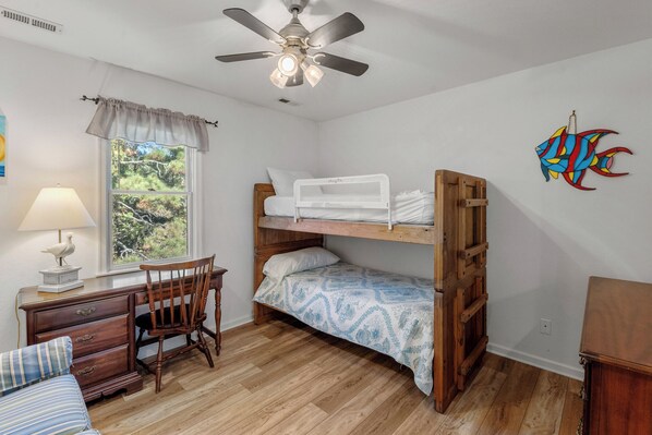 A room with a bunk bed, a desk with a chair, a lamp, and a window with a view of trees. - Heron Comes the Sun: Soundside, Pet-Friendly w/ Private Pool and Club Amenities (Corolla)