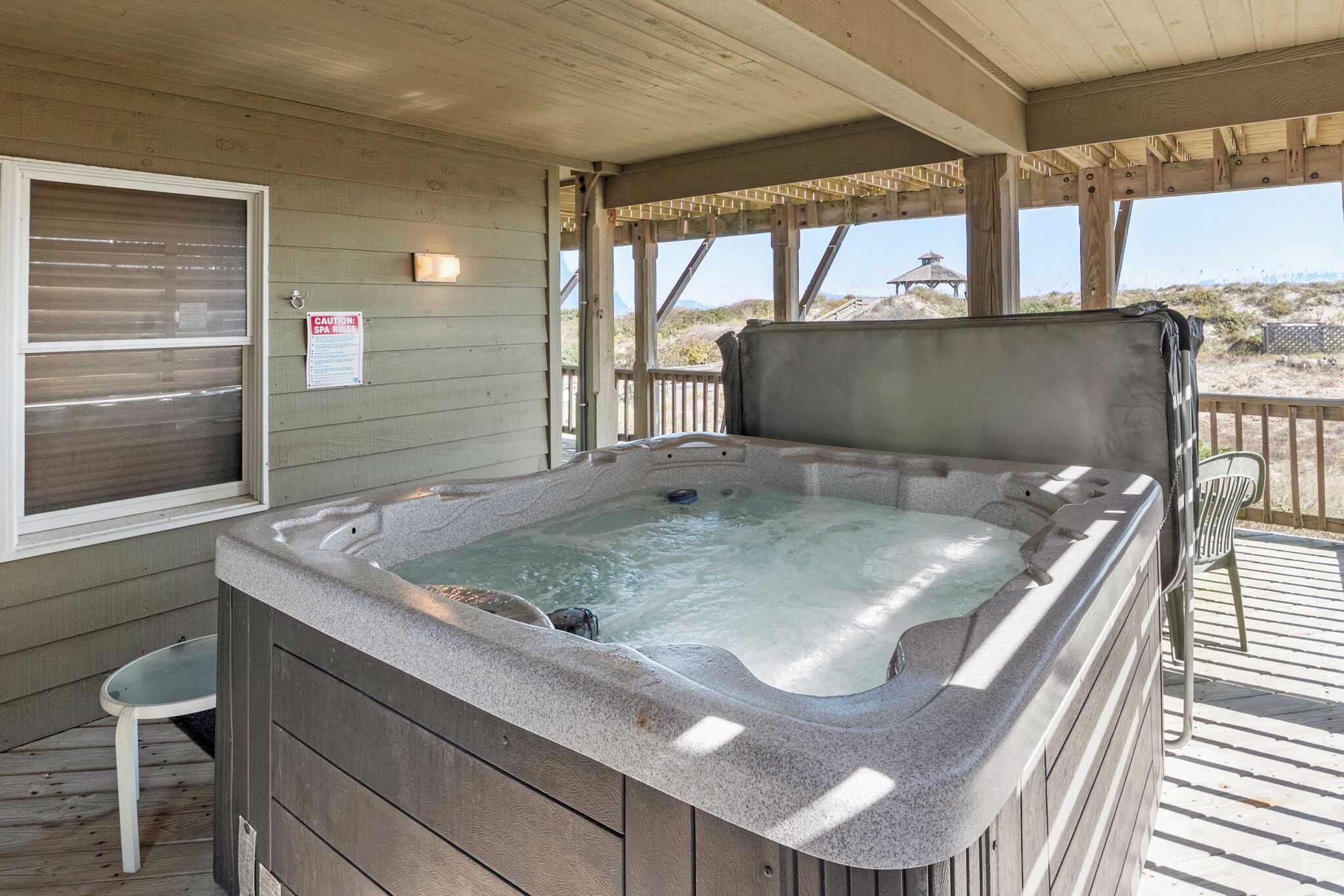 Een hottub in een overdekte buitenruimte met houten wanden en uitzicht op het strand.