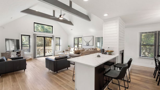 A spacious living area with a large island, dark sofas, and a fireplace. - Inspect2Sea: Pool, Hot Tub | Walk to Downtown Duck (Duck)