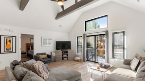 A spacious living room with a high ceiling, a flat-screen TV, and a sliding glass door leading to an outdoor area. - Inspect2Sea: Pool, Hot Tub | Walk to Downtown Duck (Duck)