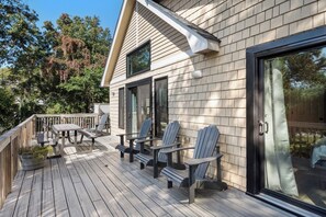 Une terrasse en bois avec des fauteuils Adirondack et une table, une porte-fenêtre coulissante et une petite fenêtre au-dessus de la porte.