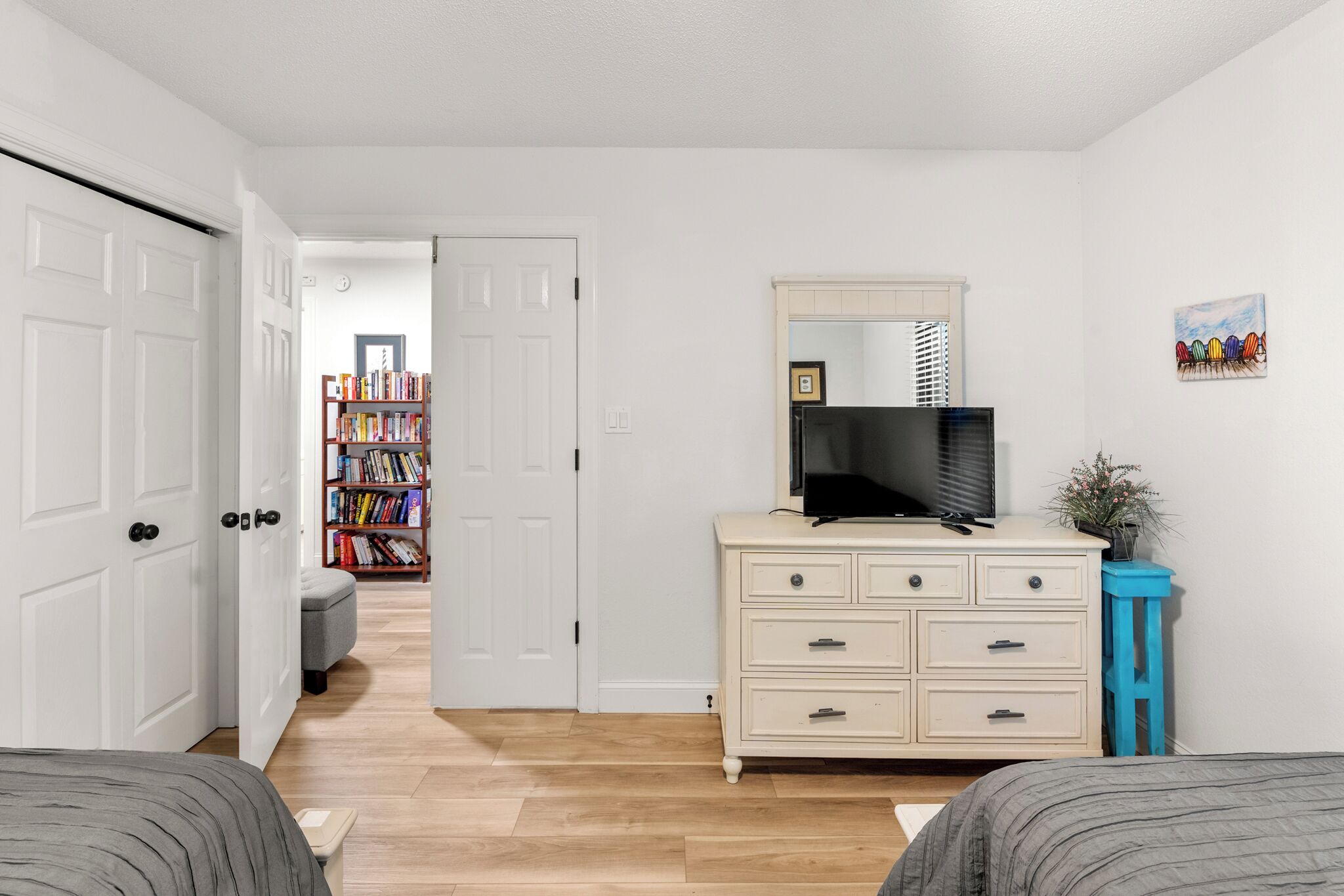 A bedroom with a bed, a dresser, a television, and a bookshelf in the background.