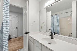 Une salle de bain avec un lavabo blanc, un grand miroir et un rideau de douche.