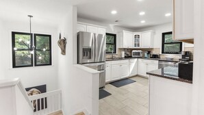 A modern kitchen with white cabinets, stainless steel appliances, and a large island. - Inspect2Sea: Pool, Hot Tub | Walk to Downtown Duck (Duck)