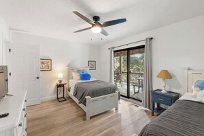 Une chambre à coucher comprenant un lit, un ventilateur de plafond, une table de chevet avec une lampe, une commode et une porte-fenêtre coulissante donnant sur un balcon.