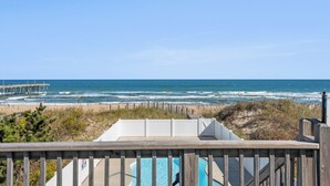 Uitzicht op een strand met een houten terras, een zwembad en een pier op de achtergrond.