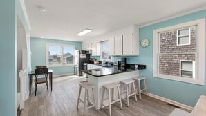 Een moderne keuken met witte kastjes, een centraal eiland met krukken en uitzicht op buiten door een raam.