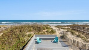 Eine Holzterrasse mit zwei Stühlen mit Blick auf einen Strand.