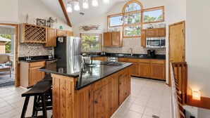 A spacious kitchen with wooden cabinets, a large island, and a view of the outdoors. - Lighthouse Jewel: Private Pool/Hot Tub/Sound Views (Corolla)