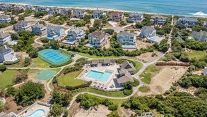 An aerial view of a residential area with houses, a tennis court, a swimming pool, and a beach in the background. - Sea Spot: Saltwater Pool, Hot Tub, Beach Club Access (Corolla)