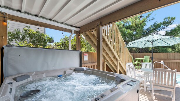 Un jacuzzi con cubierta de madera, mobiliario exterior y una escalera de madera.