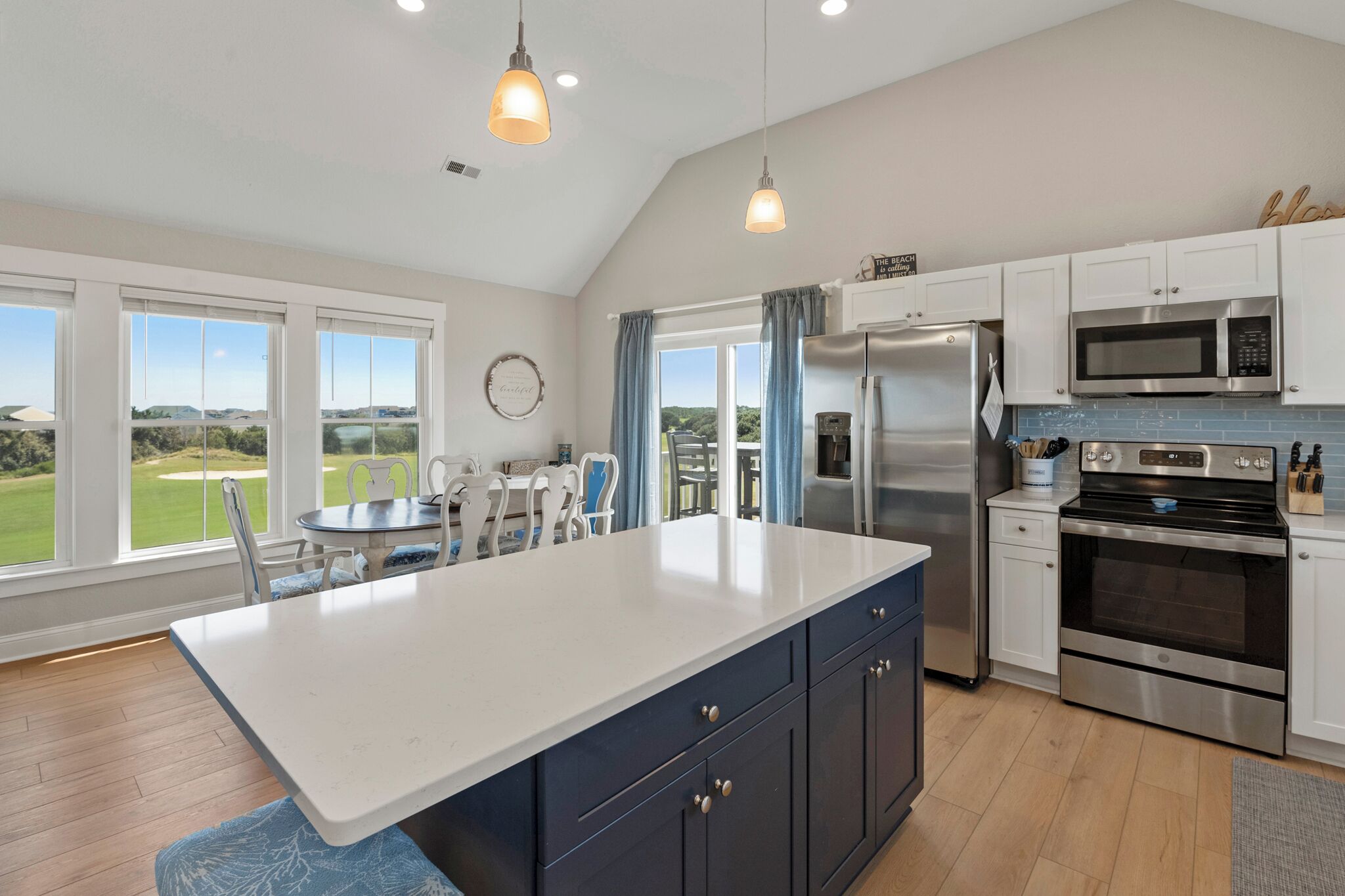 A modern kitchen with a large island, stainless steel appliances, and a view of the outdoors.