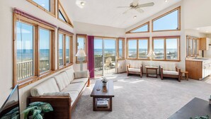 A spacious living room with large windows, a ceiling fan, and a view of the ocean. - Chirality: Oceanfront | Direct Beach Access (Duck)