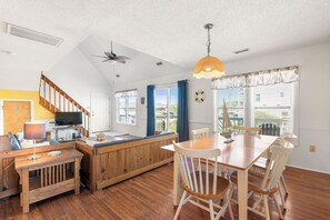 A spacious kitchen with a wooden island, a dining area with a table and chairs, a ceiling fan, and large windows with curtains.