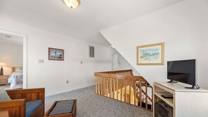 A spacious living room with a high ceiling, a wooden staircase, a television, and two framed artworks. - It's A Shore Thing: Ocean Views | Hot Tub | Dogs OK (Rodanthe)