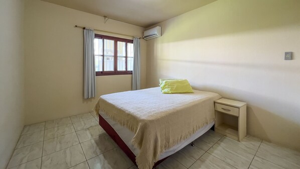 Un dormitorio con cama, mesita de noche, ventana con cortinas y equipo de aire acondicionado.