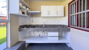 A compact kitchen with a gas stove, white cabinets, and a window with bars. - AP 09 Ala Morrinhos Residencial Solavir (Bombinhas)