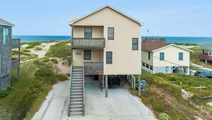 Et toetagers hus med balkon, trappe op til øvre etage og udsigt til strand og hav.