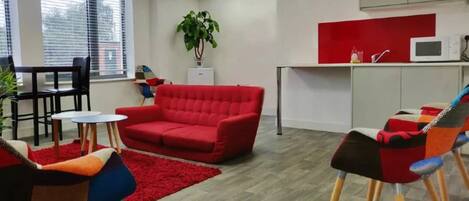 A modern office space with a red sofa, colorful chairs, a small table, and a kitchenette.