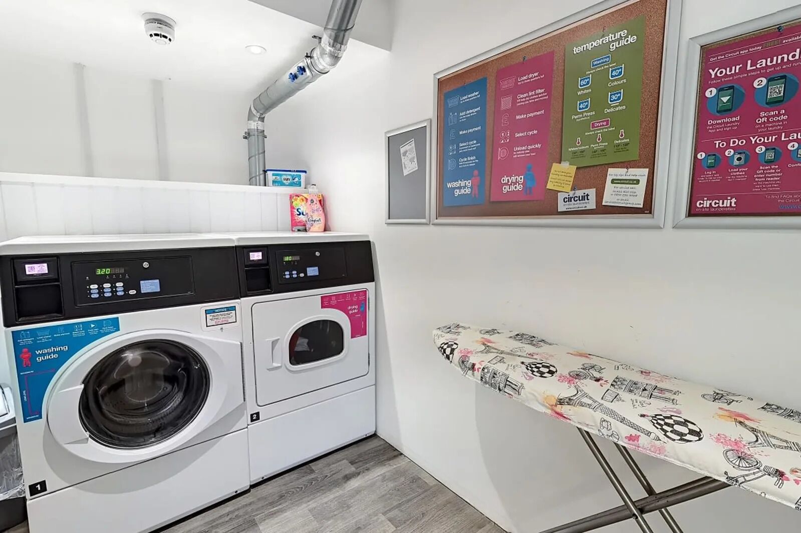 A laundry area with a washing machine, drying rack, and instructional posters on the wall.