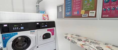 A laundry area with a washing machine, drying rack, and instructional posters on the wall.