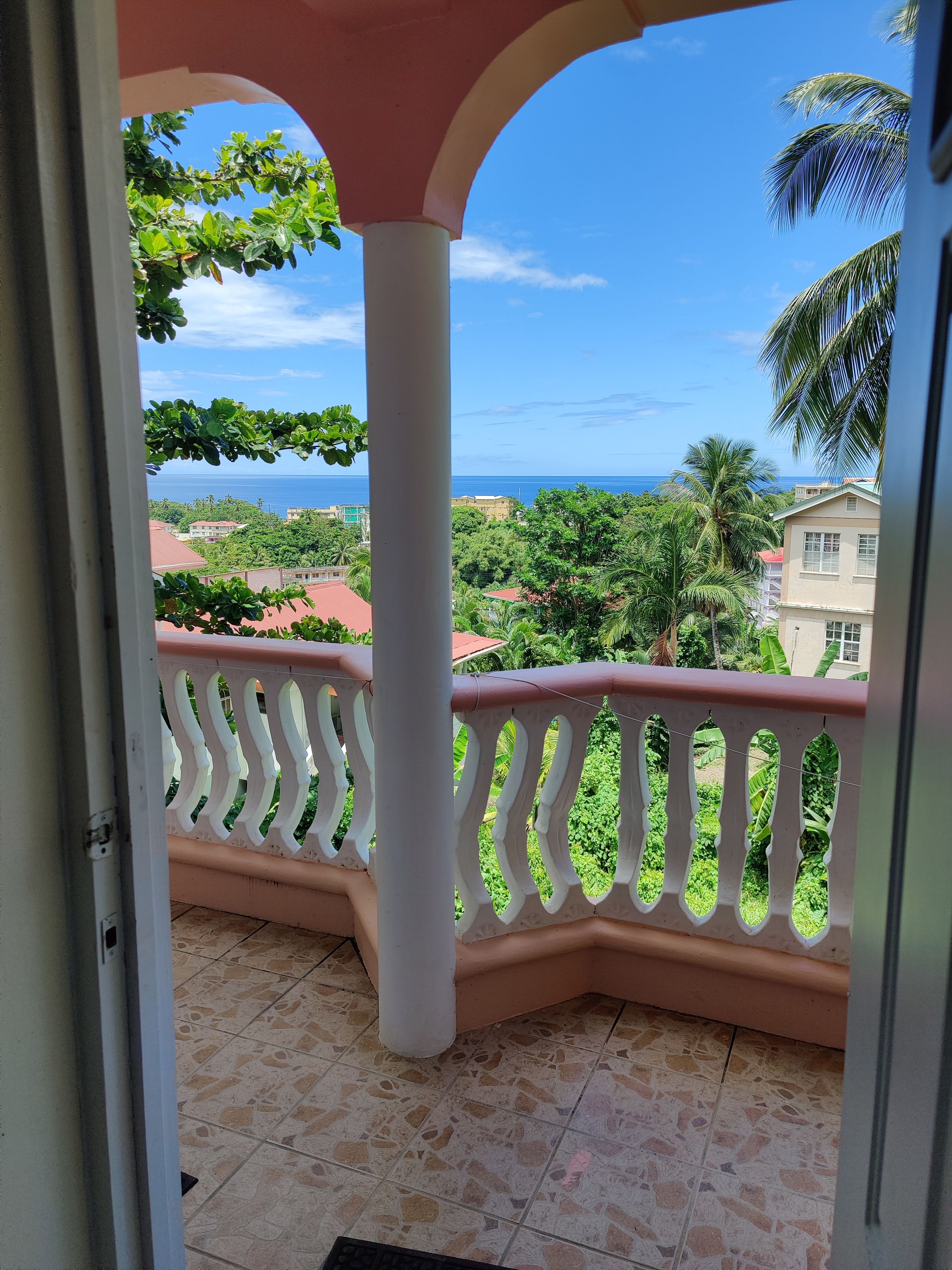 A balcony with a view of a coastal area, including buildings and greenery.