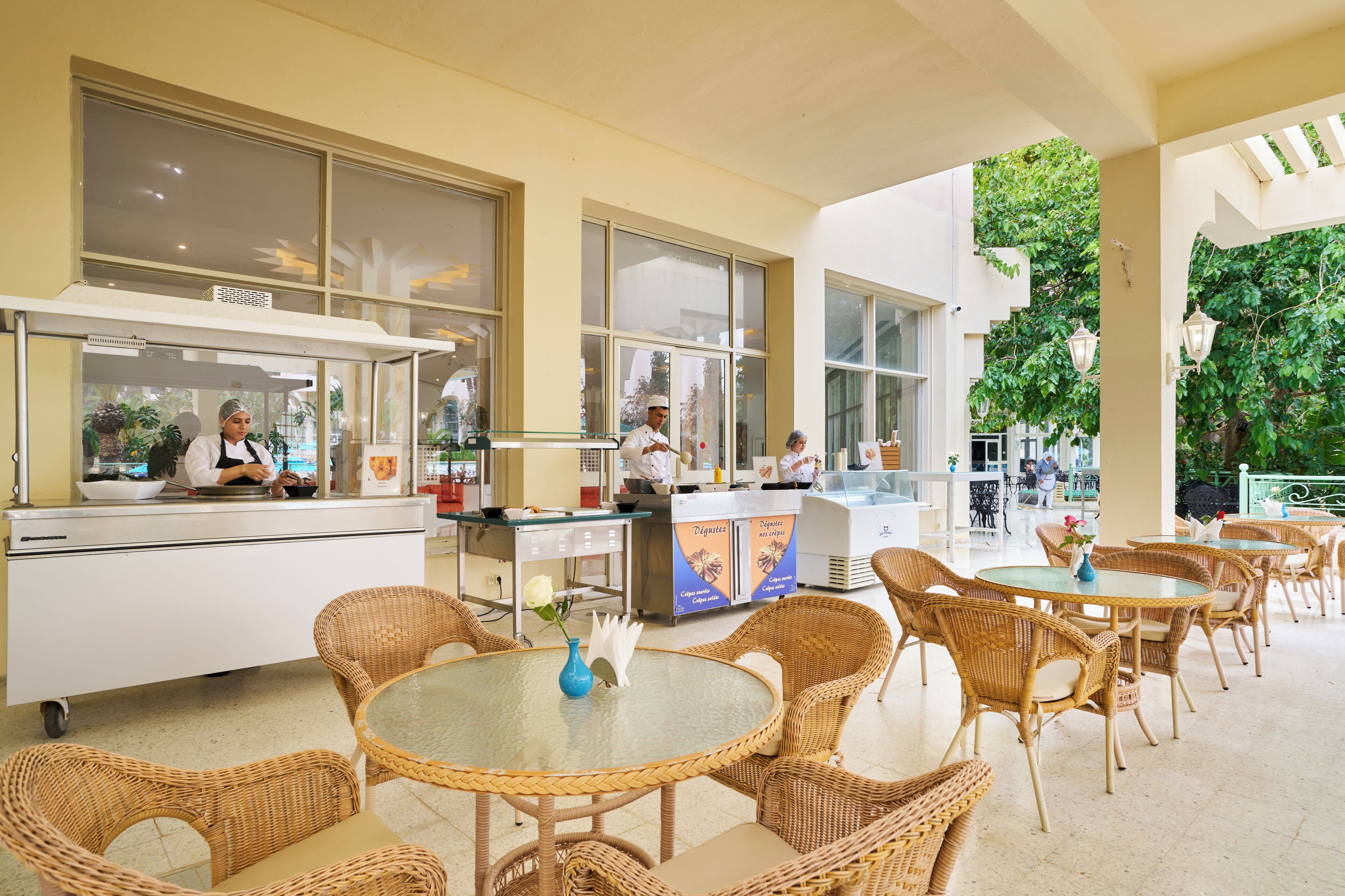A restaurant with wicker tables and chairs, a counter with staff, and large windows.