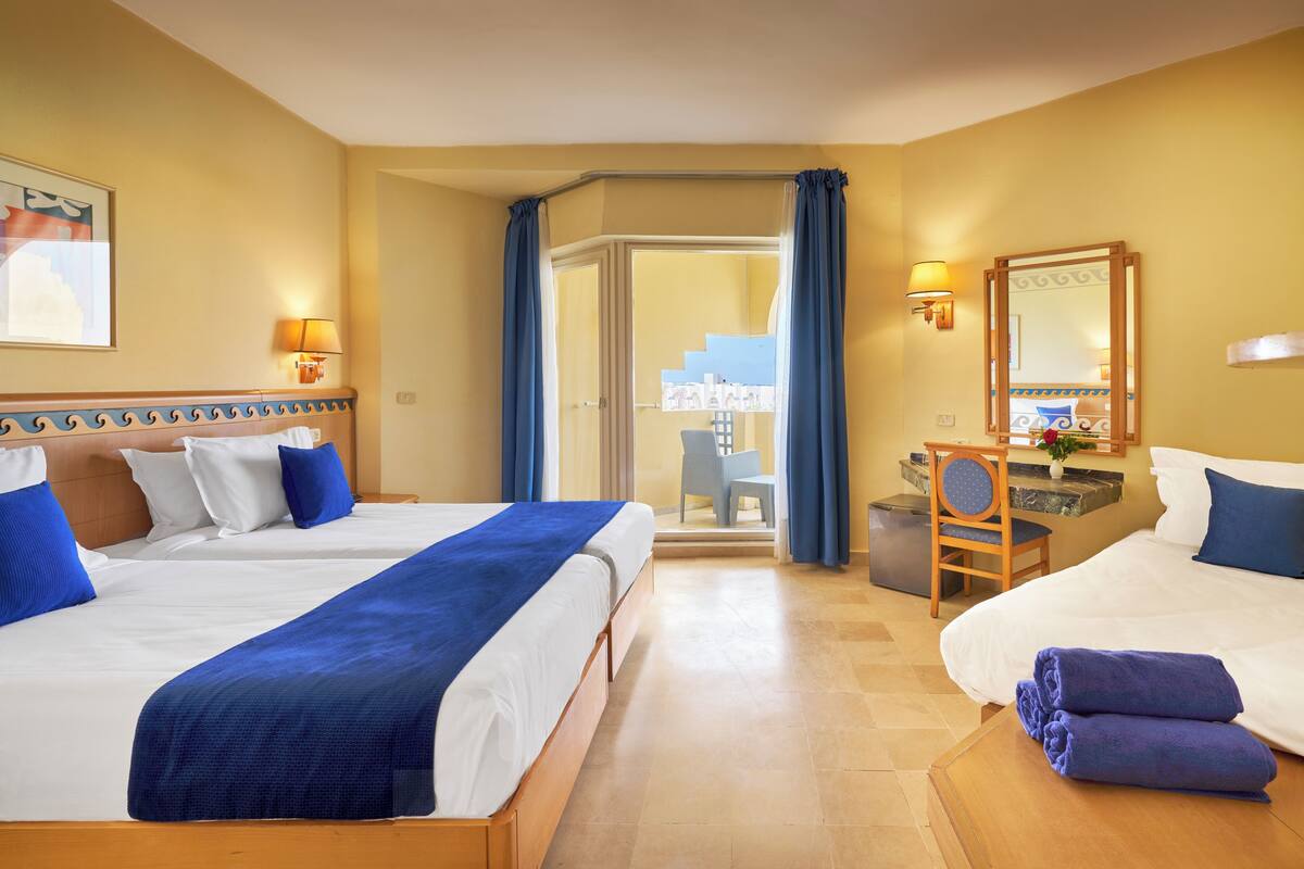 Une chambre d’hôtel avec deux lits, un bureau, une chaise, un miroir et une vue sur l’extérieur.