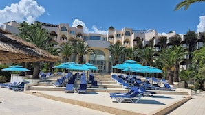 Ein Resort mit Poolbereich, ausgestattet mit Liegestühlen und Sonnenschirmen, umgeben von Palmen und einem Gebäude im modernen architektonischen Stil.