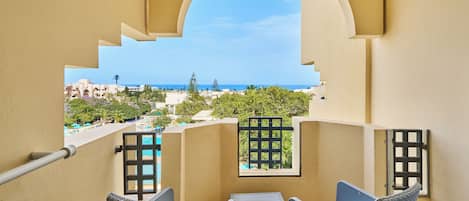 A balcony with wicker furniture, a view of the sea, and a pool area in the background.