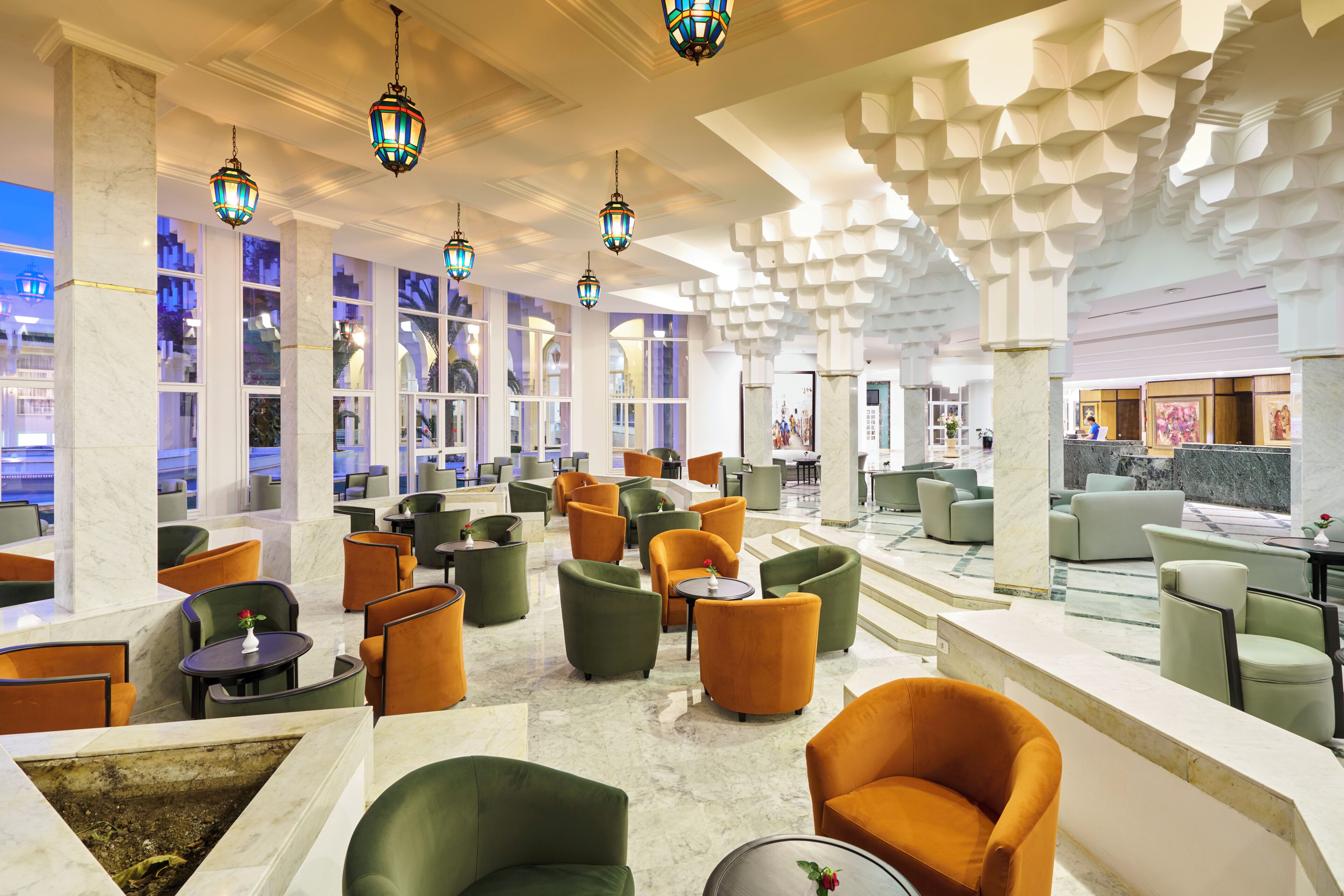 A spacious lobby with multiple seating areas, large windows, and decorative hanging lights.