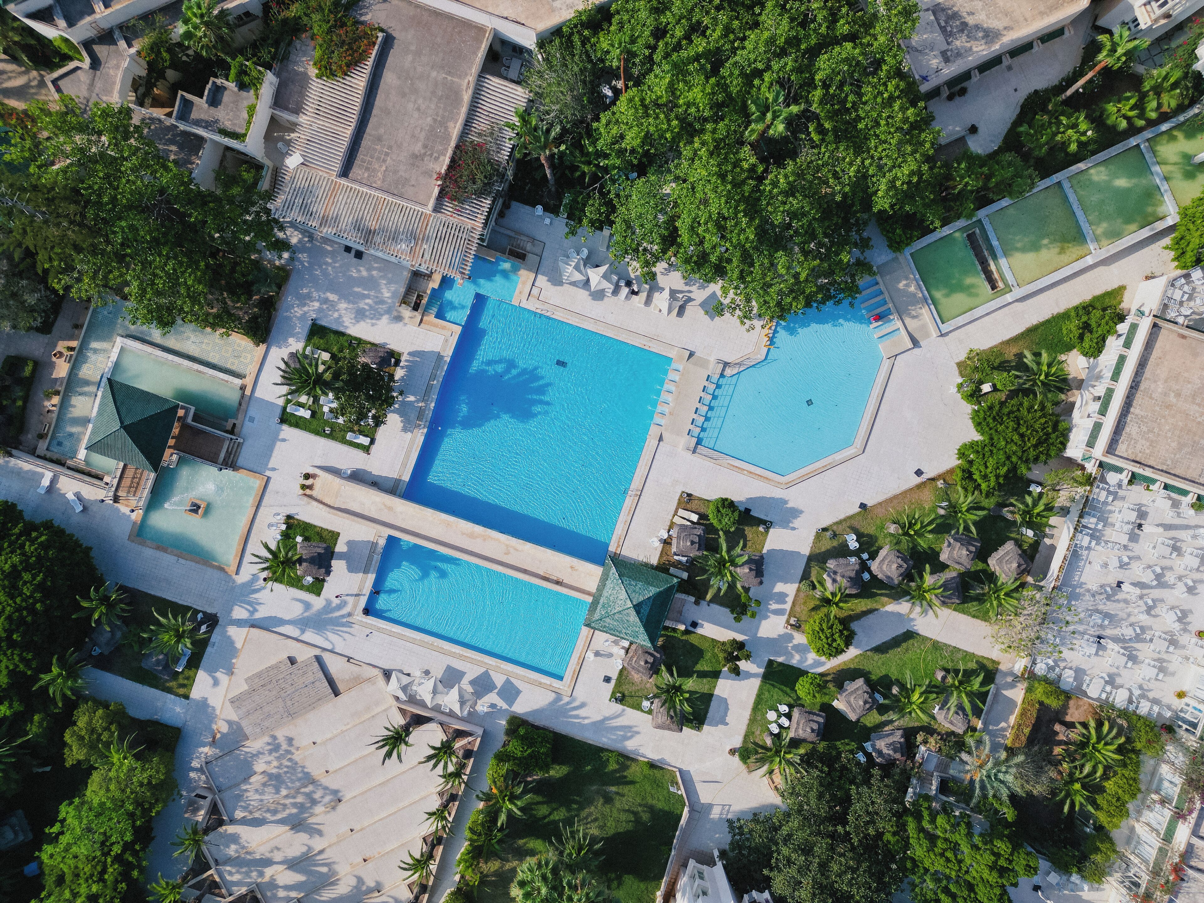An aerial view of a resort with two swimming pools, surrounded by palm trees and lounge areas.