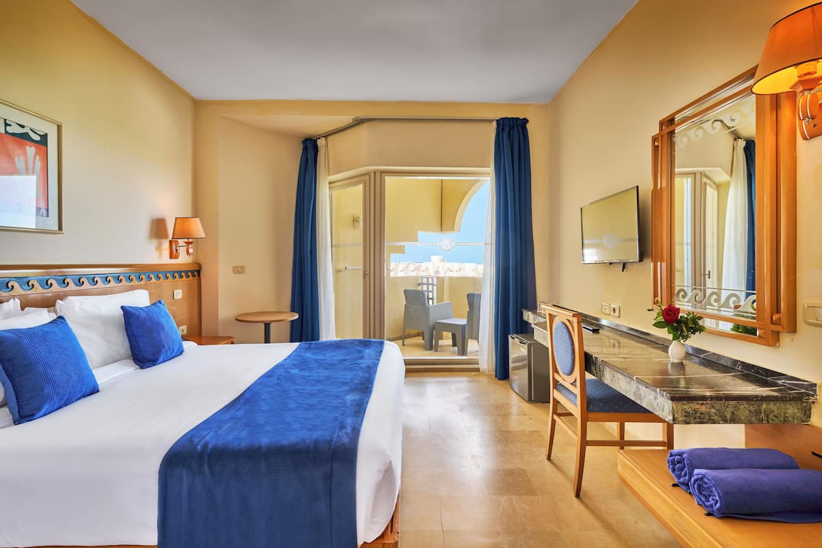 Une chambre d’hôtel avec un grand lit, un bureau, une chaise, une salle de bain avec un miroir et une vue sur l’extérieur.