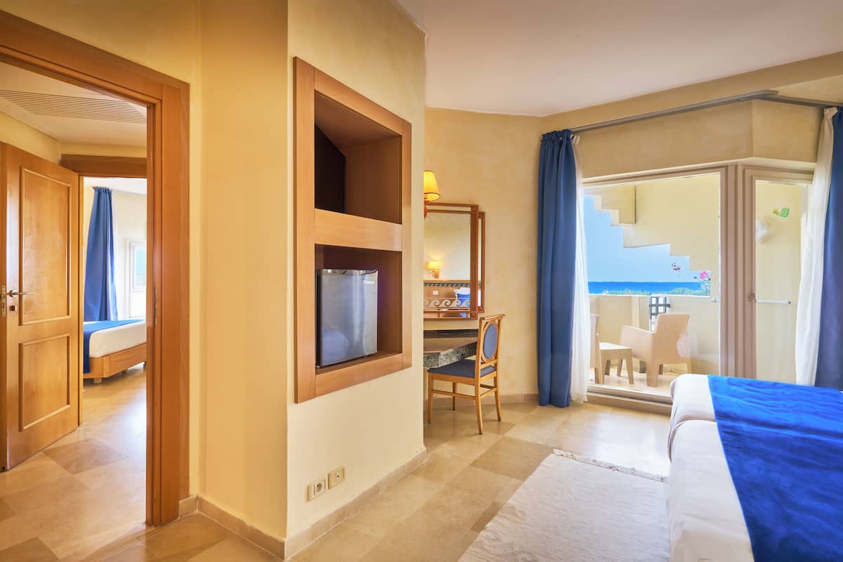 Une chambre d’hôtel comprenant un lit, un bureau avec une chaise, une fenêtre avec des rideaux et un balcon avec une chaise.