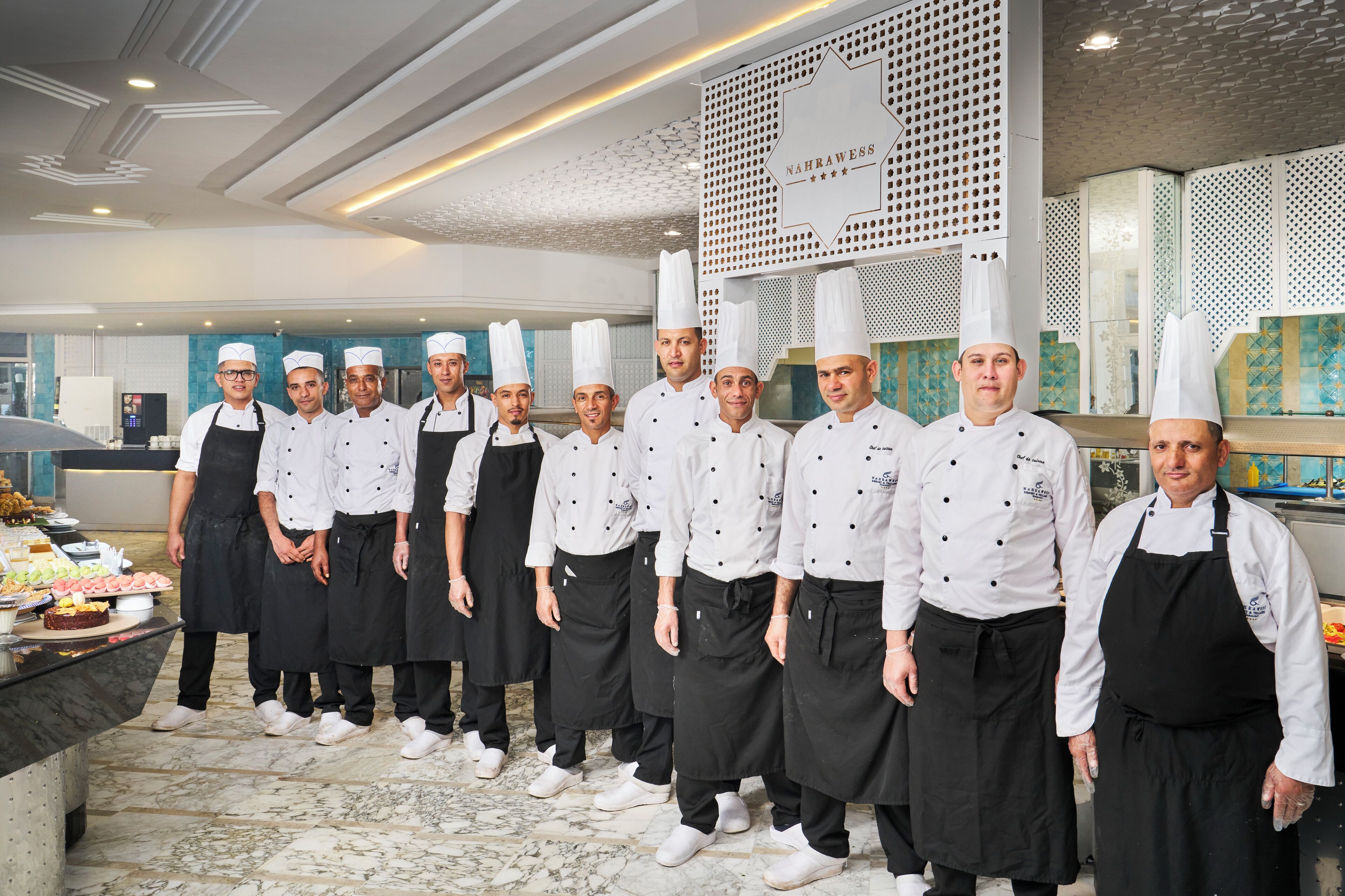 Un groupe de chefs dans une cuisine moderne, avec un mur décoratif et un sol en marbre.