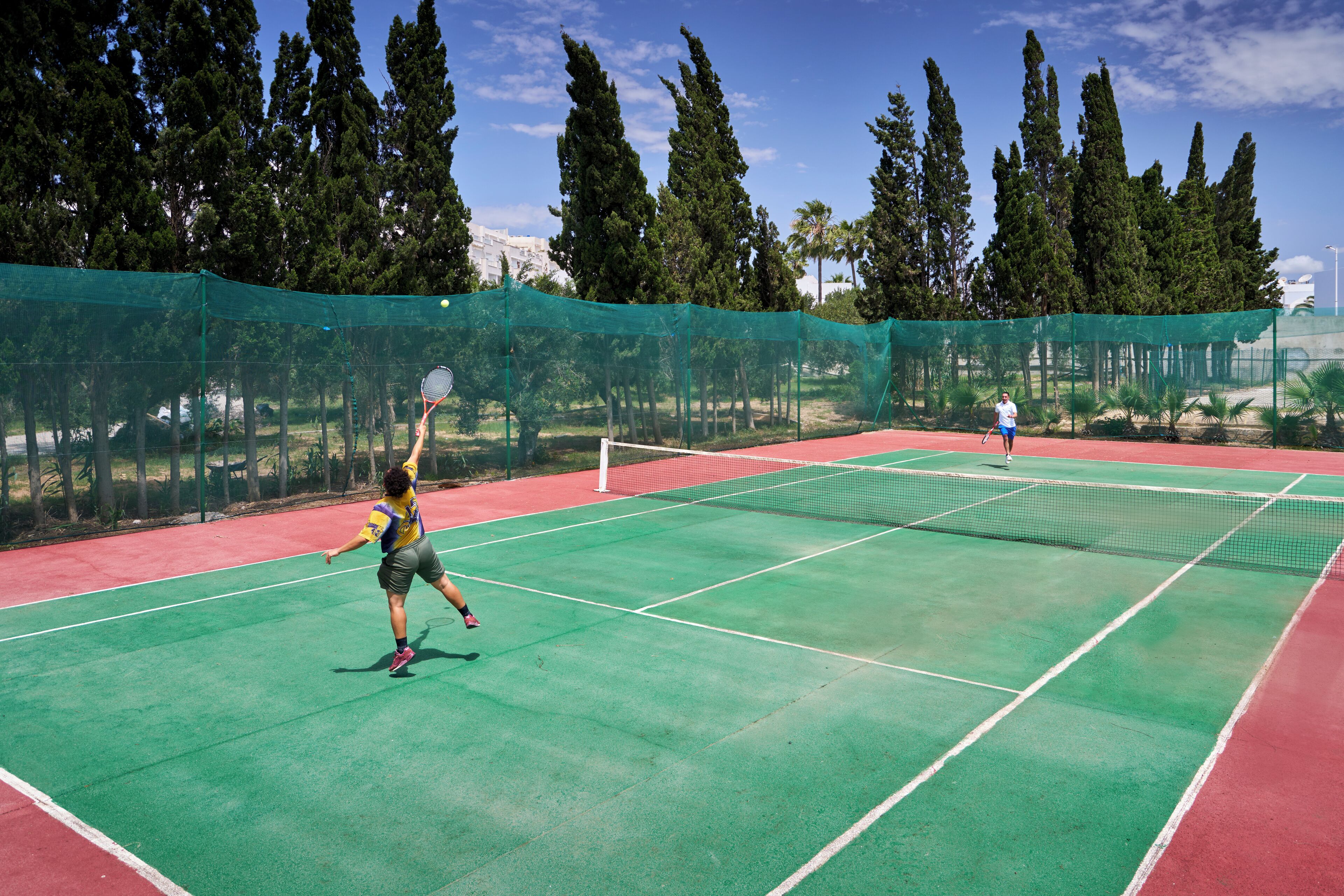 Una cancha de tenis con una red, rodeada de árboles y un cielo despejado.