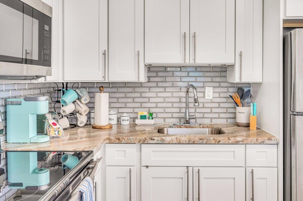 A modern kitchen with white cabinets, a granite countertop, a stainless steel sink, and a coffee maker.