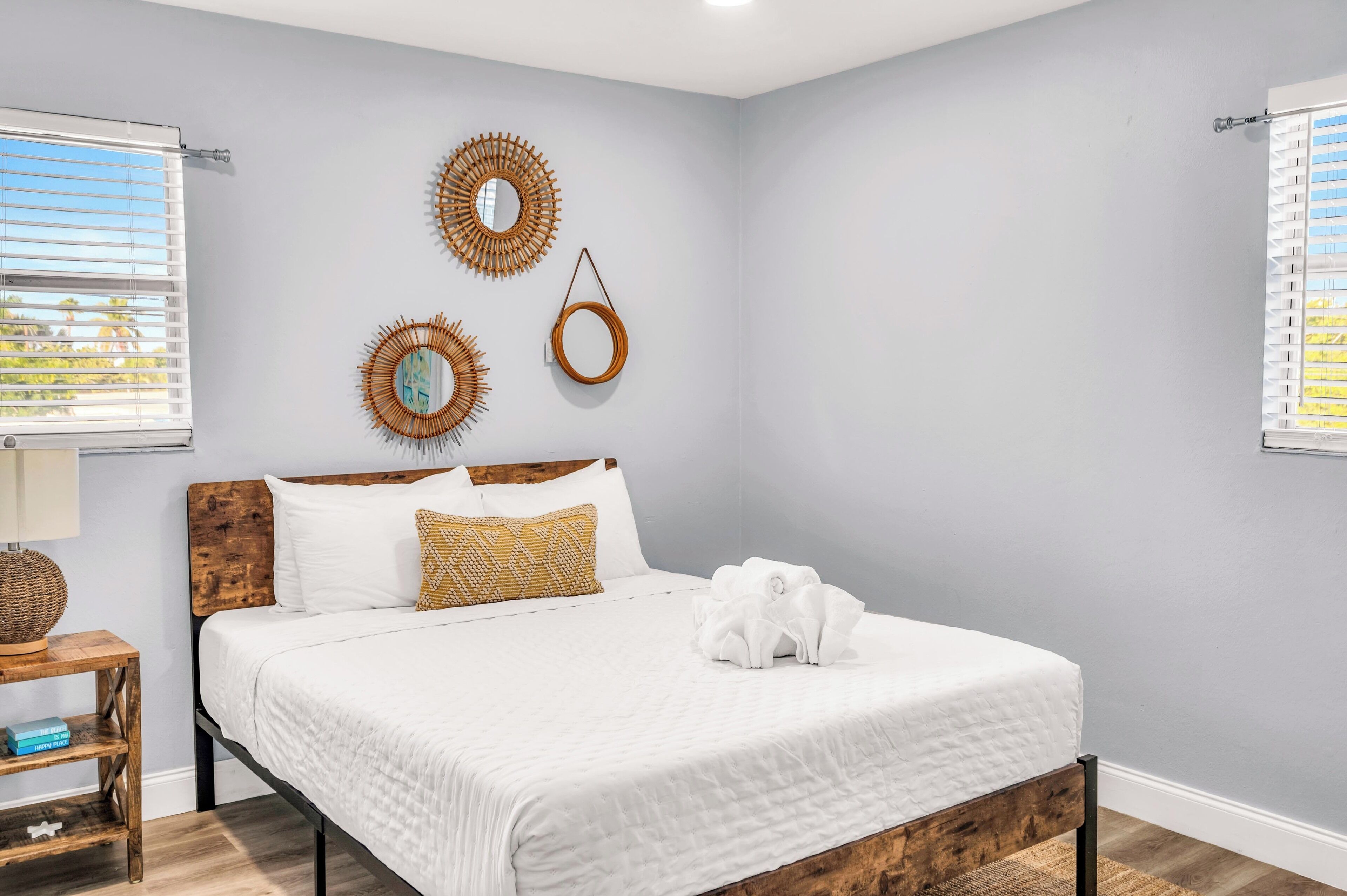 A neatly arranged bedroom with a wooden headboard, a white bedspread, and three wall-mounted decorative mirrors.