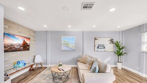 A modern living room with a wooden floor, a beige sofa, a round coffee table, and a large flat-screen TV mounted on the wall. - Seahorse Suites #3. Island Living at it's Best! (Sanibel)