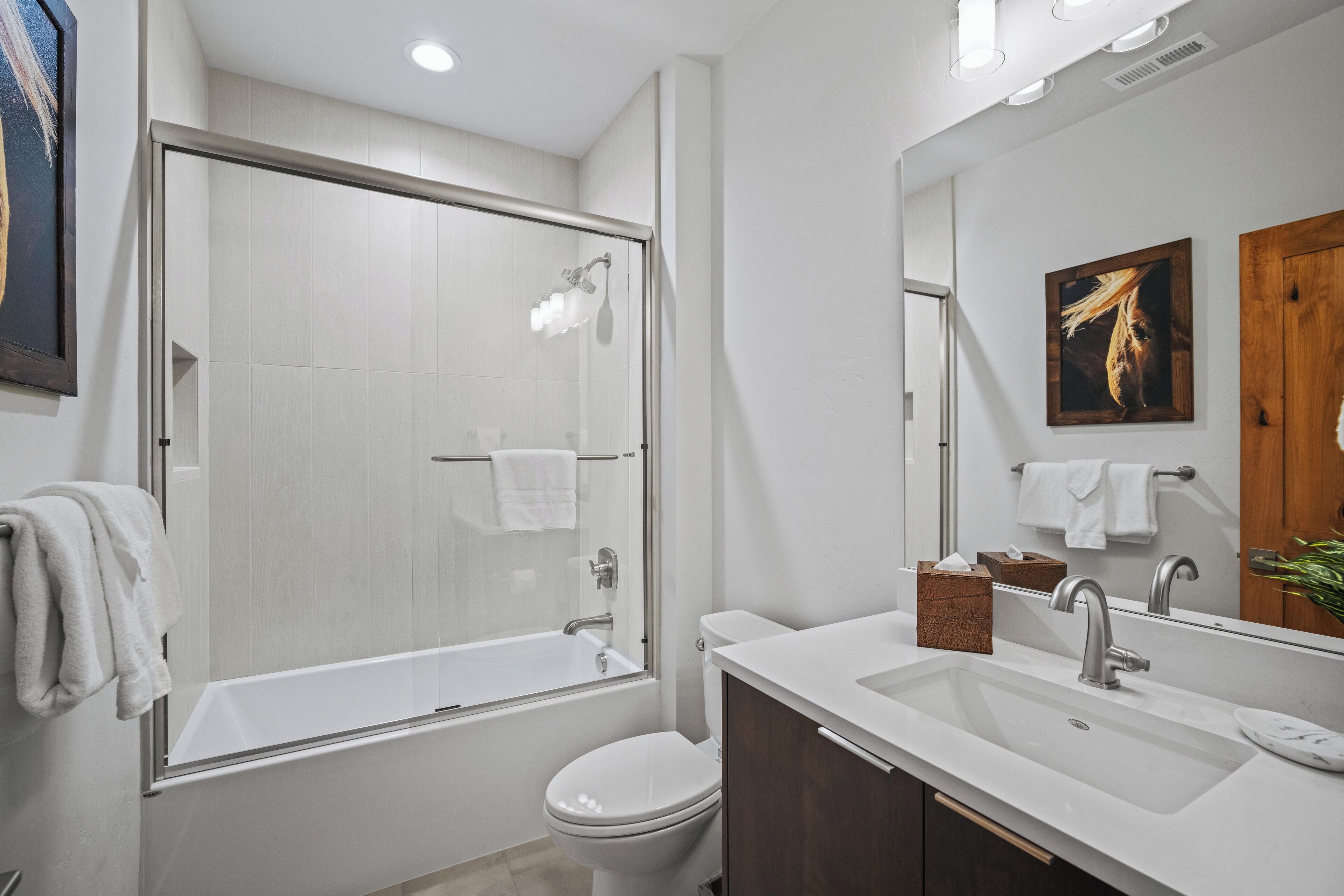 A modern bathroom with a glass-enclosed shower, a white toilet, a sink with a mirror, and a wooden cabinet.