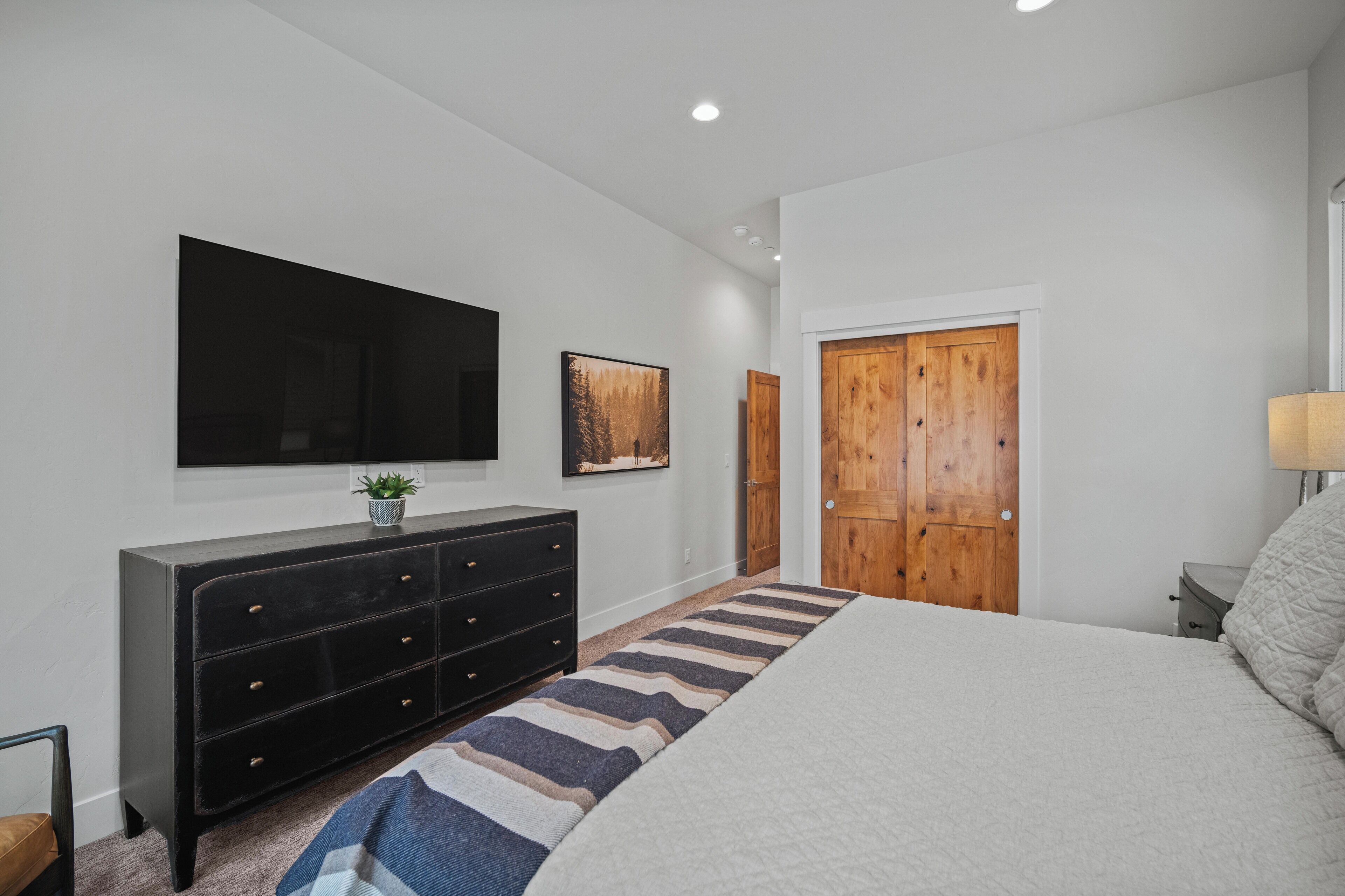 A bedroom with a bed, a dresser, a TV mounted on the wall, and a wooden door.