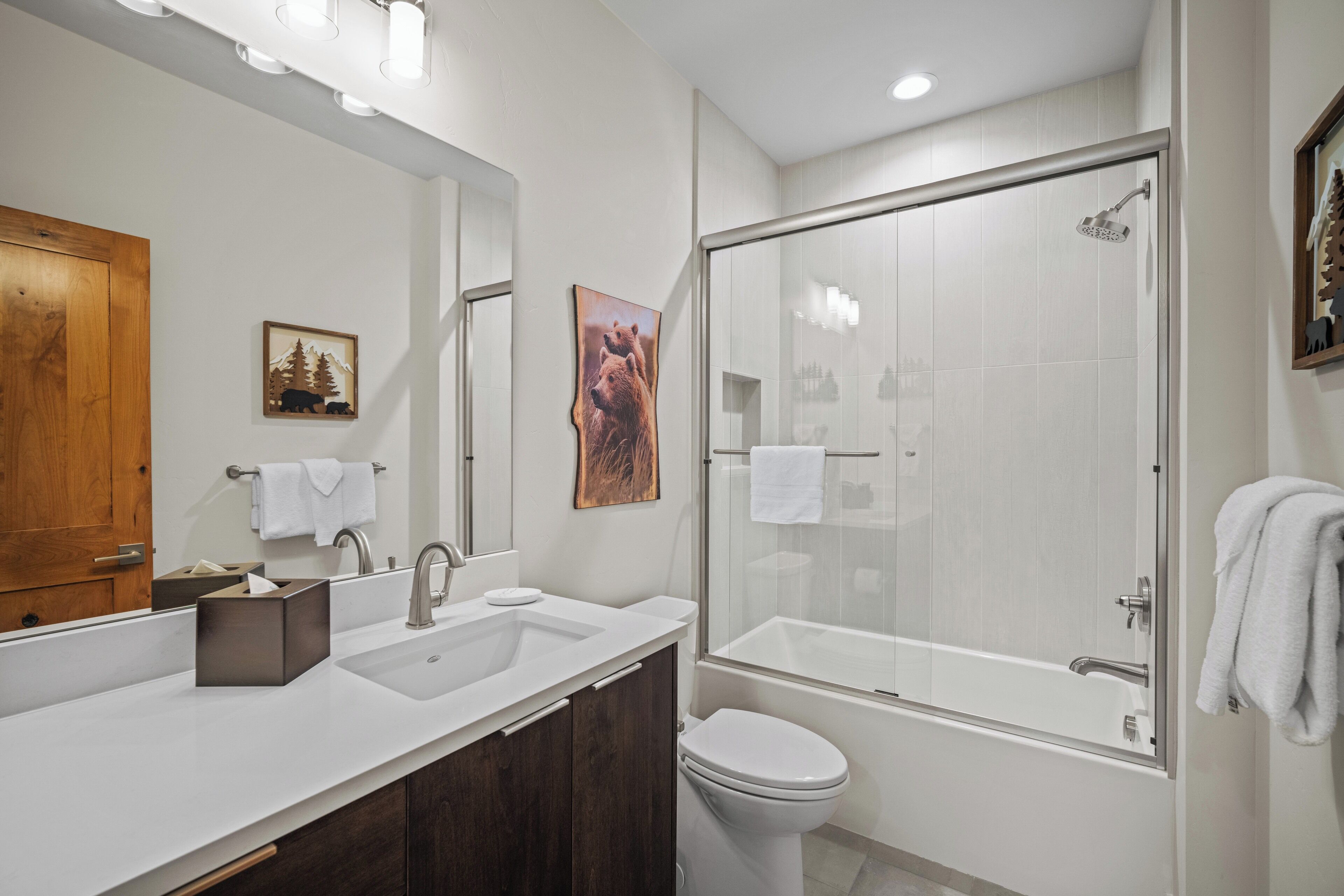A modern bathroom with a large mirror, a sink, a toilet, and a glass-enclosed shower.
