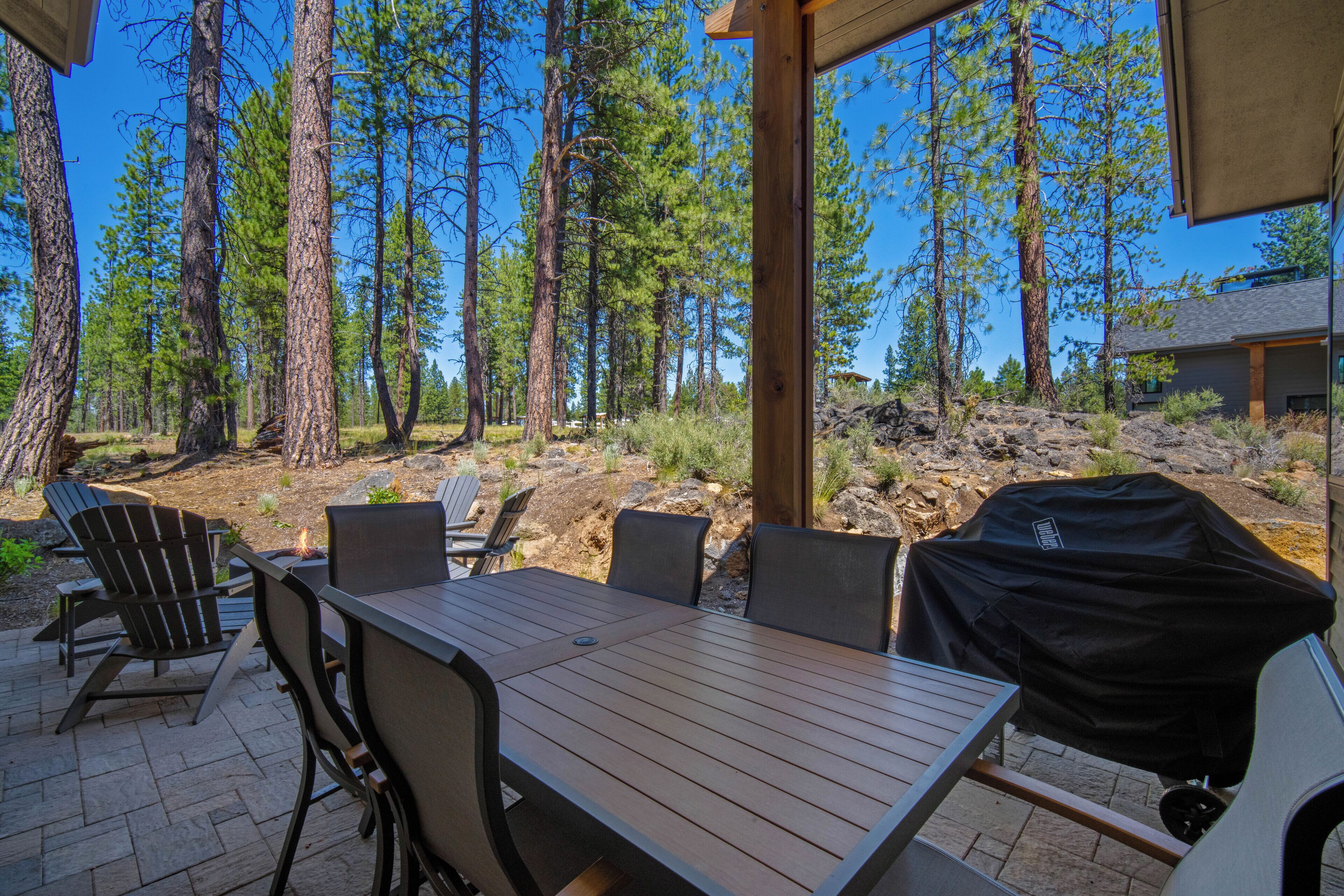 Un patio al aire libre con mesa y sillas de madera, rodeado de altos pinos.