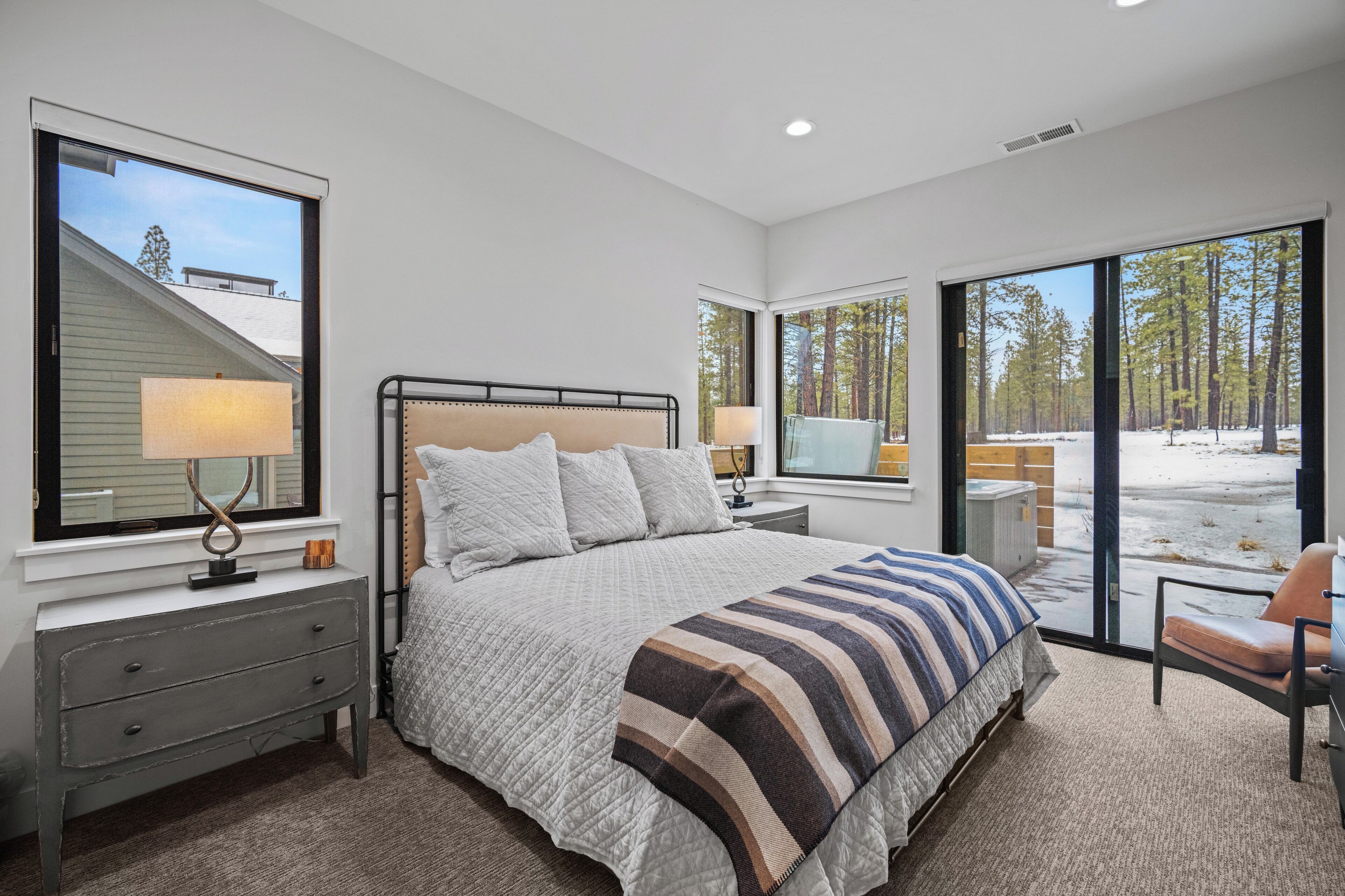 A bedroom with a bed, bedside tables, and a view of a snowy landscape through large windows.
