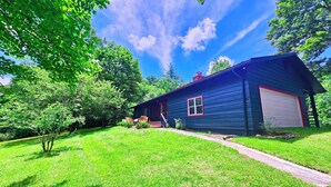 A single-story house with a garage, surrounded by lush green grass and trees. - The Marigold Cottage: Serene Mountain Getaway w/ Fire Pit, Large Yard (Highlands)