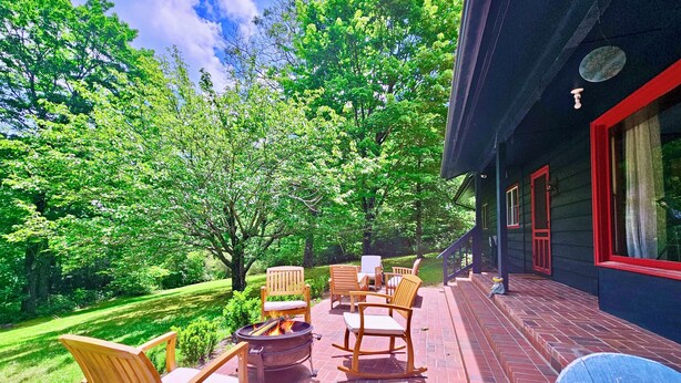 A patio with outdoor furniture, a fire pit, and a view of a lush garden and trees. - The Marigold Cottage: Serene Mountain Getaway w/ Fire Pit, Large Yard (Highlands)