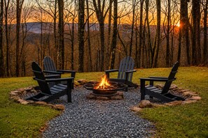 A campsite with a fire pit, four Adirondack chairs, and a gravel path.